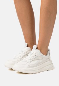 Weiße Sneakers mit einem Obermaterial aus strukturiertem Leder, gepolstertem Kragen und dicker Gummisohle; verfügen über eine runde Zehenpartie und ein schnürbares Design mit minimalen Akzenten.