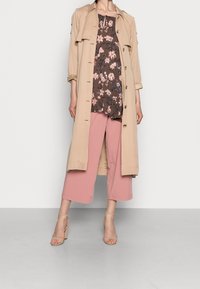 Beige trenchcoat med frontknapper, blomsterfarvet brun top og lyserøde cropped bukser. Klare hæle fuldender outfittet. Glat tekstur hele vejen igennem.