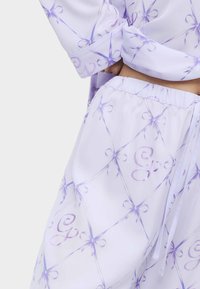 Lavendelfarbenes Pyjama-Set mit einem karierten Muster aus Schleifen und geschwungenen Buchstaben, aus glattem Stoff gefertigt, mit einem elastischen Bund und Bändern.