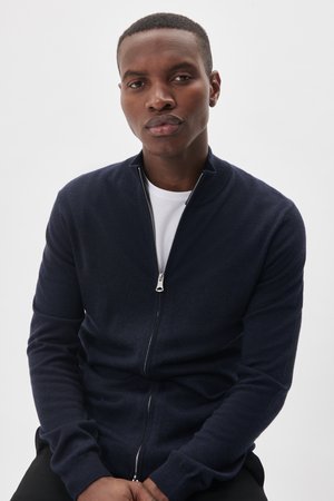 Navy zip-up cardigan made from soft knit fabric, with a stand collar and long sleeves. Features a silver zipper and ribbed cuffs.