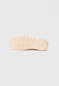 Beige Nike-kengän pohja, jossa näkyy urapohjakuvio ja kohokuvioitu Nike-swoosh vaaleanharmaalla taustalla.