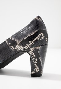 Černo-bílé střevíce na vysokém podpatku s hadím vzorem, které mají strukturovaný kožený svršek, špičatou špičku a robustní blokový podpatek.