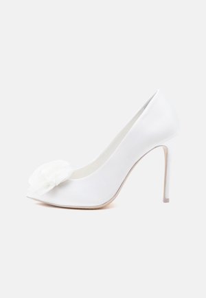 Chaussure à talon haut en satin blanc avec bout pointu, talon stiletto et grande fleur décorative en tissu sur le devant.