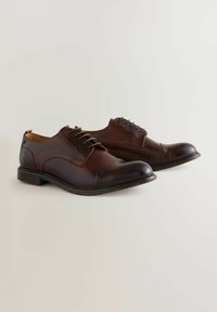 Chaussures habillées en cuir marron, avec un bout arrondi, un laçage, et des accents texturés, comportant un talon bas et des coutures contrastantes.