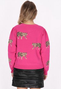 Rosa Strickpullover mit einem sich wiederholenden Tiger-Muster in Schwarz und Beige. Das Design umfasst einen Rundhalsausschnitt und lange Ärmel.
