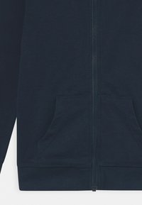 Námornícky zip-up mikina vyrobená z mäkkej tkaniny, s centrálnym zipsom, dvoma prednými vreckami a rebrovými manžetami a lemom.