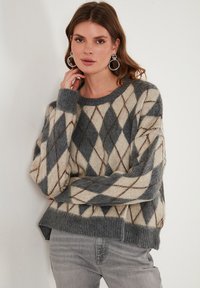 Chunky pleten pulover v sivi in bež barvi z argyle vzorcem, z običajnim okroglim izrezom in rebrastimi manšetami. Mehak volneni blend material.