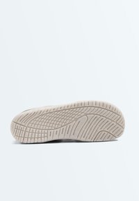 Semelle de chaussure avec un motif de bande de roulement texturé, présentant des rainures intersectées et un ovale central marqué "ONSYO" sur un fond clair.