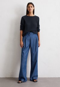 Marineblauer strukturierter Strickpullover mit umgeschlagenen Ärmeln, kombiniert mit weit geschnittenen hellblauen Hosen, die mit einer Knopfleiste vorne und einem lässigen Schnitt ausgestattet sind.