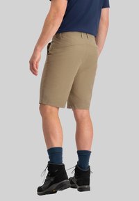 Beige Shorts aus leichtem Stoff, mit geradem Schnitt, Gesäßtaschen und kombiniert mit schwarzen Wanderschuhen sowie dunkelblauen Socken.