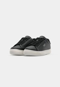 Baskets en cuir noir avec une semelle en caoutchouc, bout rond et lacets plats. Présente un branding subtil sur la languette et sur le côté. Texture lisse.