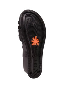 Suela de zapato negra con goma texturizada y patrones ondulados. Un destacado logo en forma de asterisco naranja está centrado en la suela.