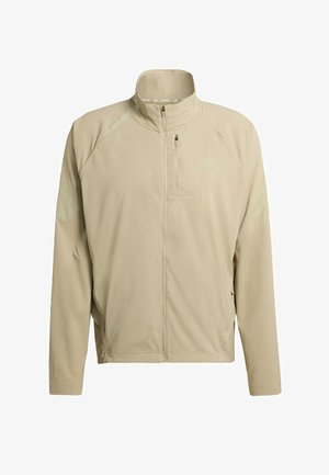 Veste de course beige avec un col haut, fermeture éclair sur toute la longueur et deux poches latérales ; présente des logos discrets et une texture de tissu respirant.