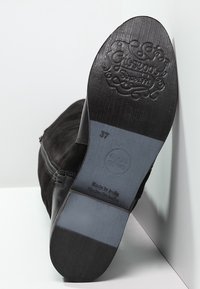 Stivale alla caviglia in suede nero con suola in gomma testurizzata, caratterizzato da un logo sagomato e taglia 37 sulla soletta. Dettaglio con zip laterale.