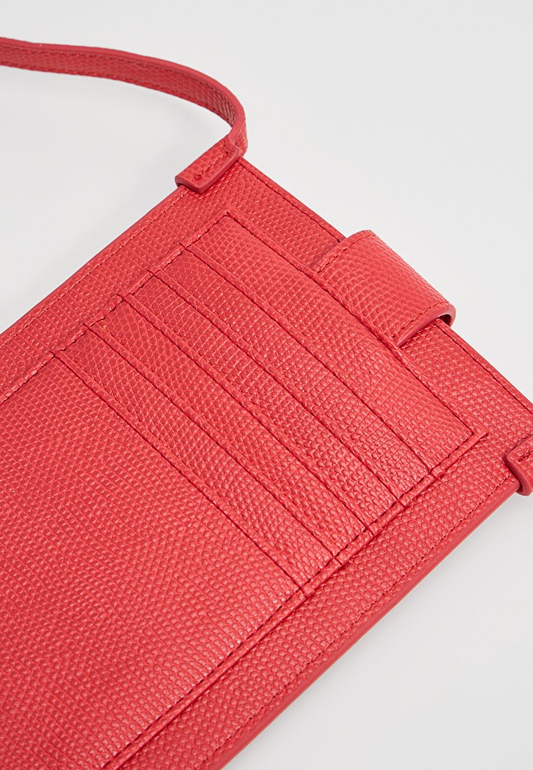 Cartera roja texturizada con una correa, que cuenta con cinco espacios para tarjetas y un cierre de lengüeta. El material tiene un acabado en relieve para un mejor agarre.
