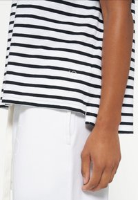 Camisa de manga corta a rayas en blanco y negro fabricada en tejido suave, con un dobladillo con aberturas laterales y un pequeño detalle de logo cerca de la parte inferior.