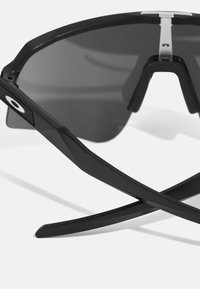Ochelari de soare negri cu un design sleek și unghiular. Lentile întunecate, ramă din plastic și accente metalice pe puntea superioară. Design ușor.