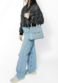 Borsa a struttura blu chiaro con patta, dettagli in oro e manici doppi. Abbinata a una giacca bomber nera e jeans in denim chiaro.
