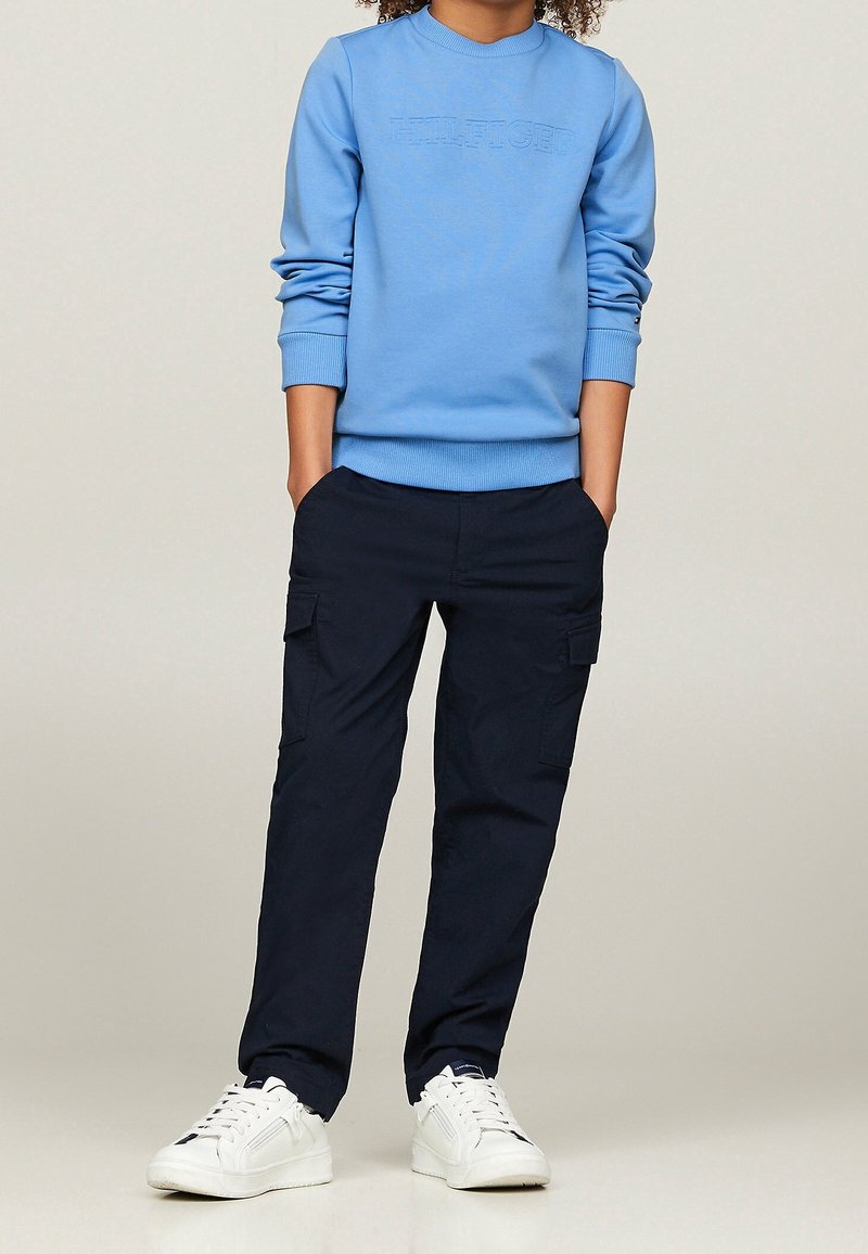 Blauwe katoenen sweatshirt met een reliëflogo, gecombineerd met marineblauwe cargobroeken met zijzakken. Witte sneakers maken de outfit compleet.