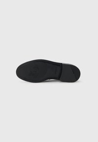 Suela de zapato de goma negra con patrón de textura. Presenta un detalle de logo en relieve y un borde suave para mayor agarre y estabilidad.