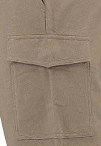 Pantaloni cargo beige con una grande tasca a pattina. Il tessuto ha una texture liscia e dettagli di cucitura sottili.