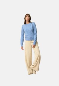 Jasnoniebieski sweter w warkoczowy wzór, okrągły dekolt, detale na rękawach; w zestawieniu z szerokimi prążkowanymi spodniami w kolorze kremowym, o teksturowanej tkaninie.