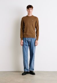 Bruine lange mouwen shirt, lichtblauwe jeans en zwarte schoenen. Eenvoudig ontwerp met een ronde hals en recht gesneden pasvorm.