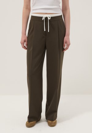 Personne portant un pantalon large vert olive avec une ceinture à cordon blanc et des chaussures beige, associé à un haut blanc sans manches.