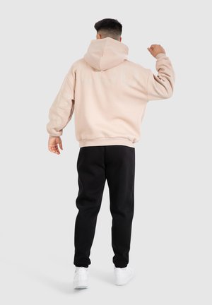 Stofroze hoodie met een groot logo op de achterkant, geribbelde manchetten en zoom, gecombineerd met zwarte joggingsbroek en witte sneakers, gezien van achteren.
