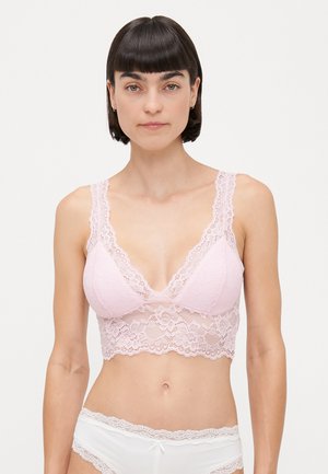 Světle růžový krajkový bralet s hlubokým výstřihem do V, květinovým vzorem, širokými krajkovými ramínky a vroubkovaným lemem, nošený s bílými spodním prádlem s krajkovým lemem.