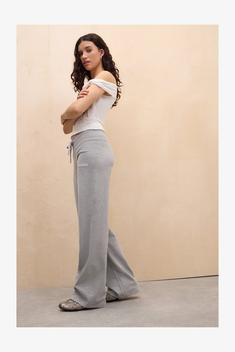 Gray loose-fitting sweatpants with a drawstring waist and logo detail. The model wears a fitted white off-the-shoulder top.