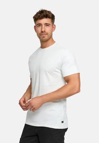 T-shirt bianca a maniche corte in cotone morbido, con scollatura rotonda e un piccolo logo. Indossata con pantaloni cargo scuri.