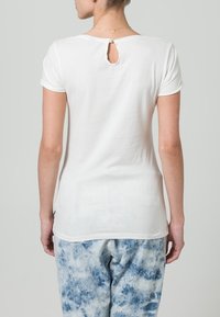 Hvid kortærmet t-shirt med rund halsudskæring og nøglehul detalje bagpå, lavet af blødt stof, parret med blå tie-dye bukser.