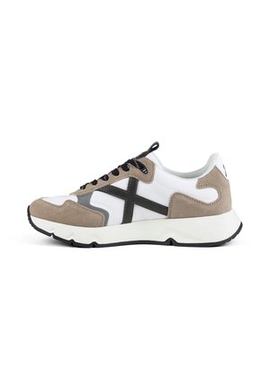 Zapatilla baja con ante blanco y beige, cordones negros, detalle lateral en cruz negro y suela gruesa blanca con dibujo negro, vista lateral sobre fondo blanco.