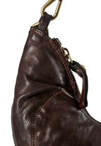 Angolo di una borsa in pelle marrone scuro con zip in ottone, tirazip e un gancio in ottone attaccato a un ciclo in pelle su uno sfondo bianco.