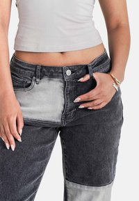Pantaloni in denim patchwork neri e grigi con vita alta, dotati di tasche frontali e chiusura con bottone metallico. Tessuto dalla texture liscia.