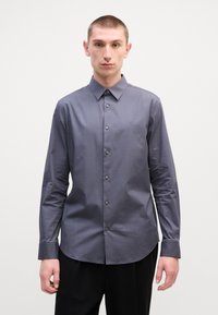 Ανδρικό πουκάμισο με μακριά μανίκια σε σκούρο γκρι, κατασκευασμένο από απαλό ύφασμα, με κλασικό γιακά, κουμπί και διακριτική λεπτομέρεια λογότυπου.