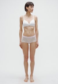 Baltas be siūlių liemenėlė su gilia iškirpte, derinama su pastelinių spalvų gėlių rašto berniukiško stiliaus šortukais, turinčiais švelniai rožinę juostelę juosmens srityje.