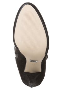 Bottine en daim noir au design élégant, avec un bout pointu et une semelle en caoutchouc beige lisse présentant de fines rainures pour une meilleure adhérence.