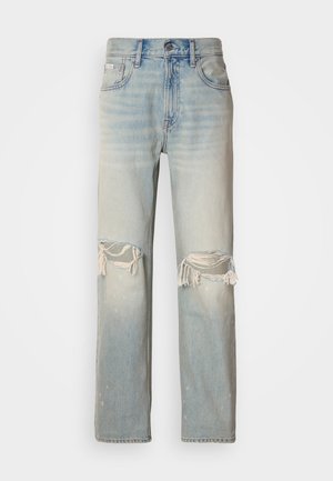 Jeans de mezclilla azul claro con cintura alta, piernas anchas y desgastes pronunciados en las rodillas. Presenta bordes deshilachados y un desvanecimiento sutil.