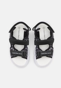 Černobílé sandály s nastavitelnými popruhy, s logem a vzorem textu. Texturovaný svršek s bílou podrážkou pro pohodlí a dobrou trakci.