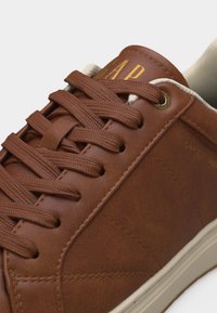 Baskets en cuir marron avec lacets assortis, logo "GAP" jaune sur la languette, et doublure intérieure ainsi que semelle rembourrées beiges.