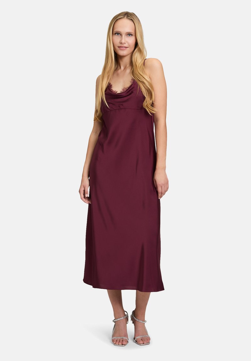 Burgunderfarbiges Satin-Maxikleid mit Cowl-Ausschnitt, verstellbaren Spaghetti-Trägern und glatter Textur; getragen mit silbernen Riemchen-Heels.