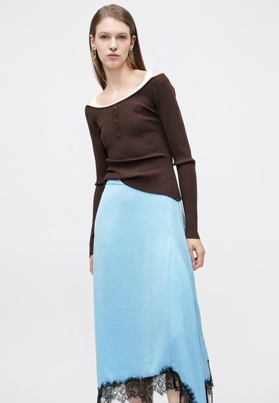 Καφέ μακρυμάνικη ριμπ μπλούζα με εκρού λαιμόκοψη και κουμπιά στο μπροστινό μέρος, σε συνδυασμό με μπλε σατέν φούστα με μαύρη δαντέλα στις άκρες.