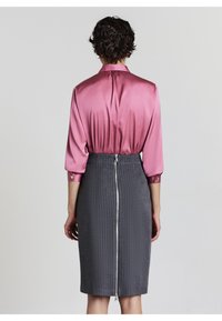 Blusa di raso rosa con maniche lunghe, abbinata a una gonna a tubino grigia a righe sottili con una chiusura lampo visibile sul retro.
