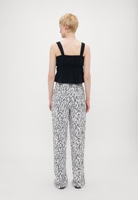Black peplum top with wide straps paired with loose-fitting white trousers featuring a black abstract pattern. Smooth texture, clean lines.