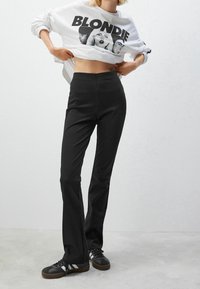 Pantalon noir taille haute associé à un sweat-shirt court blanc avec un imprimé graphique. Des baskets avec des accents noirs et argentés sont portées.