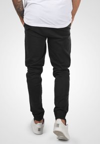 Black tapered jogger pants with an elastic waistband and cuffs, made of cotton fabric. Worn with white sneakers.
