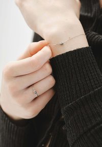 Pulsera de cadena de plata con pequeños elementos decorativos redondos. La textura es suave, llevada en una muñeca con un suéter de canalé oscuro.