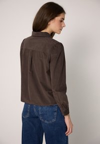 Brown corduroy shirt with a collar and buttoned cuff sleeves. Features a back yoke and a relaxed fit. Paired with blue denim jeans.